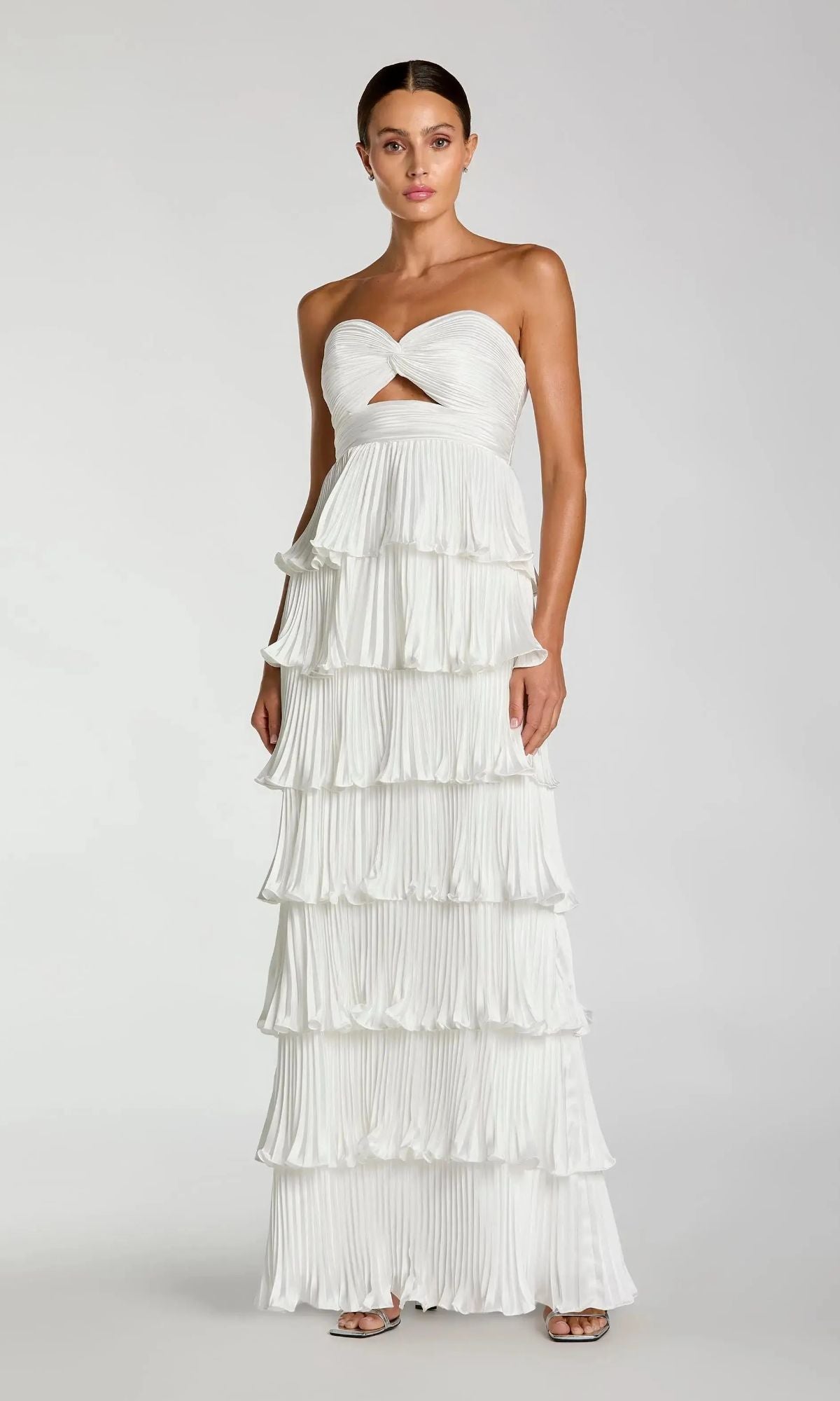Woman in an ivory Mac Duggal 49981 long formal dress featuring a strapless twist knot bodice, chest cutout, and multi-tiered pleated ruffles, posing against a plain background.